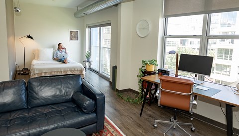a woman sits on a couch in a room with a bed and a desk